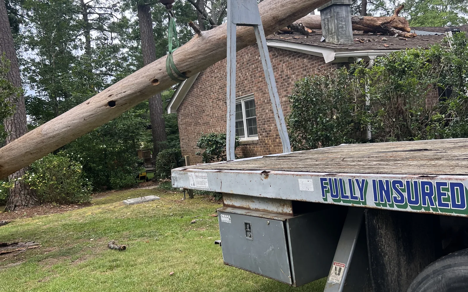 Large pine log being loaded onto Cherry's Tree Service fully insured flatbed truck beside a brick home in Greenville, NC